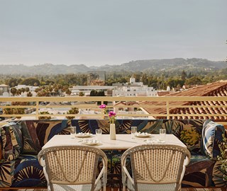 An outside table with a pink flower in a vase at a restaurant overlooking a city skyline with rolling hills and buildings.