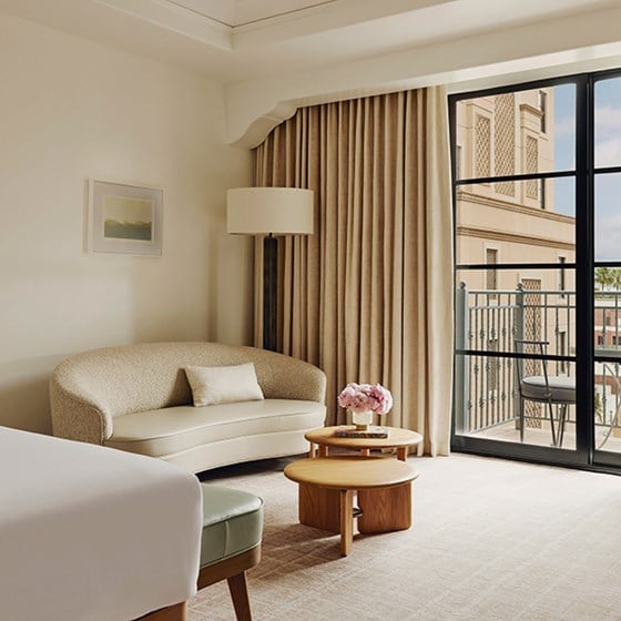 A hotel living area with a sofa and a wooden coffee table with pink flowers. There's a sliding glass door to a balcony.